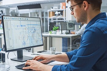 Mann arbeitet am PC in Großraumbüro.