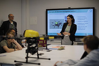 Dozenten im Unterricht mit Smart Board im Hintergrund und Drohne auf Tisch